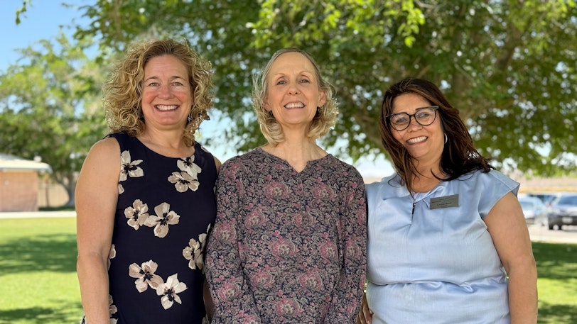 Three white women standing beside each other outside with a tree in the background